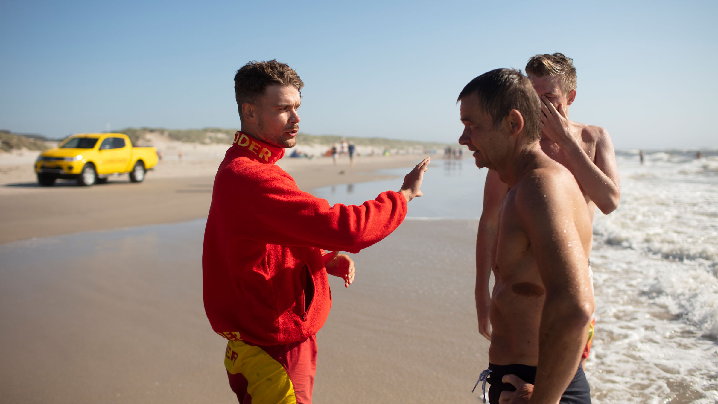 livredder taler med mænd på strand